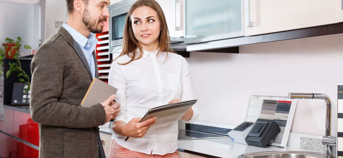 Polite  salesgirl helping young man in choice of mixer tap in kitchen furniture salon